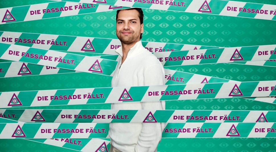 Auf dem offiziellen Kandidatenbild zu Promi Big Brother 2025 ist Jimi Blue Ochsenknecht vor einem türkisfarbenen Hintergrund mit Augen-Symbolen und dem Slogan „Die Fassade fällt.“ zu sehen.