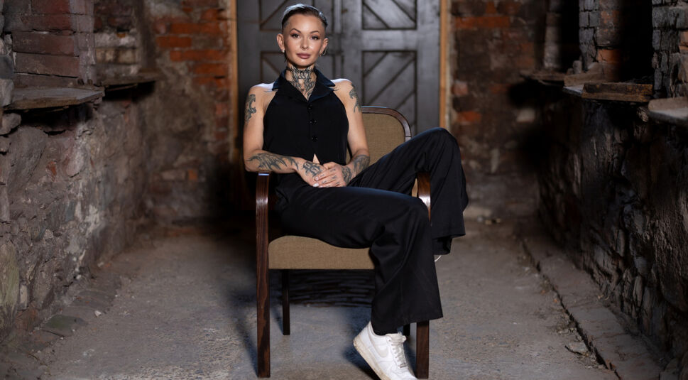 Edith Stehfest ist auf dem Bild zu „Das große Promi-Büßen“ 2025 in einem schwarzen, ärmellosen Outfit zu sehen und sitzt lässig in einem Holzsessel.