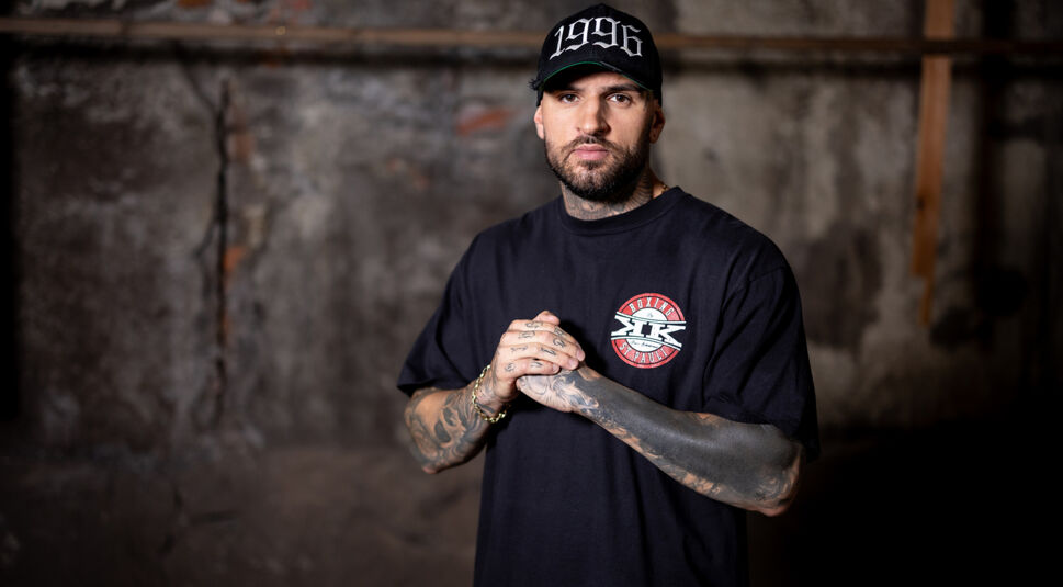 Diogo Sangre trägt auf dem Bild zu „Das große Promi-Büßen“ 2025 ein schwarzes T-Shirt und eine Cap mit der Jahreszahl 1996.