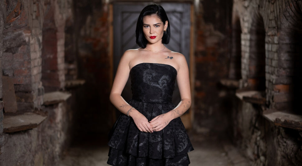 Linda Braunberger ist auf dem Bild zu „Das große Promi-Büßen“ 2025 in einem schwarzen trägerlosen Kleid mit floraler Struktur zu sehen.