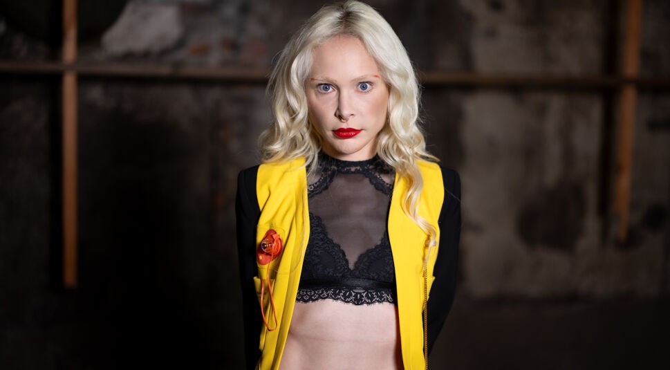 Theresia Fischer blickt auf dem Bild zu „Das große Promi-Büßen“ 2025 in die Kamera. Sie trägt ein gelb-schwarzes Outfit mit transparentem Spitzentop.