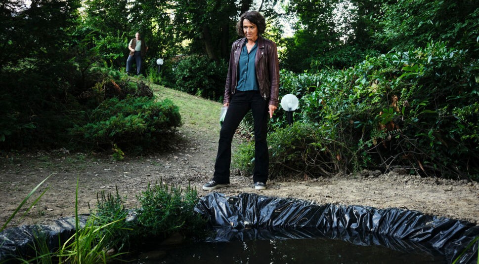 Kommissarin Lena Odenthal steht im Garten von Mikes Eltern und schaut auf den frisch angelegten Gartenteich.