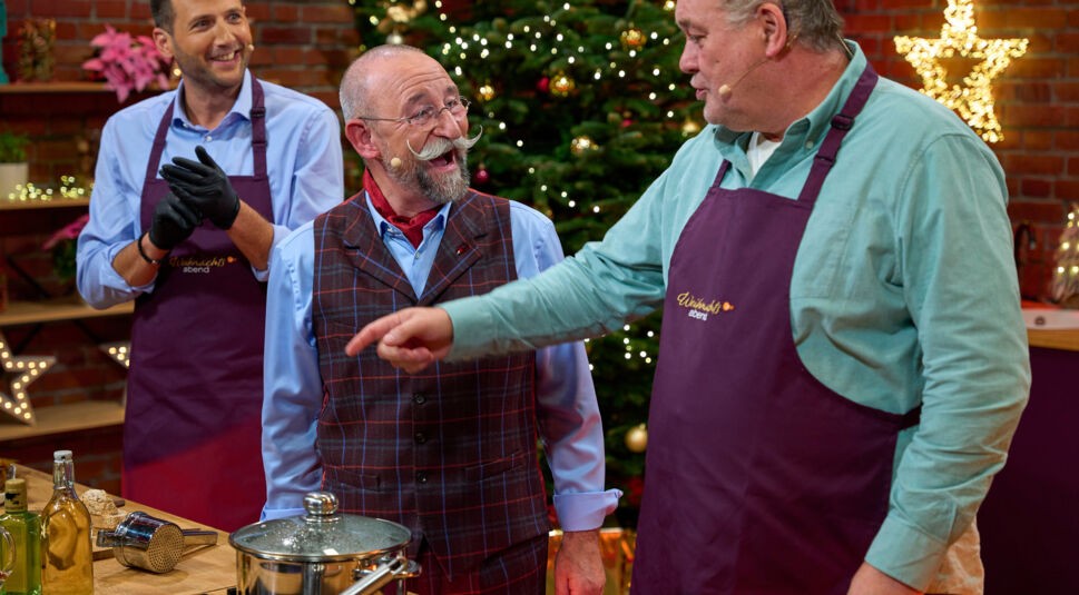 Julian Schmitz-Avila, Horst Lichter und Walter Lehnertz stehen hinter einer Küchenzeile und scherzen miteinander. Im Hintergrund steht ein Weihnachtsbaum, es hängen Weihnachtssterne.