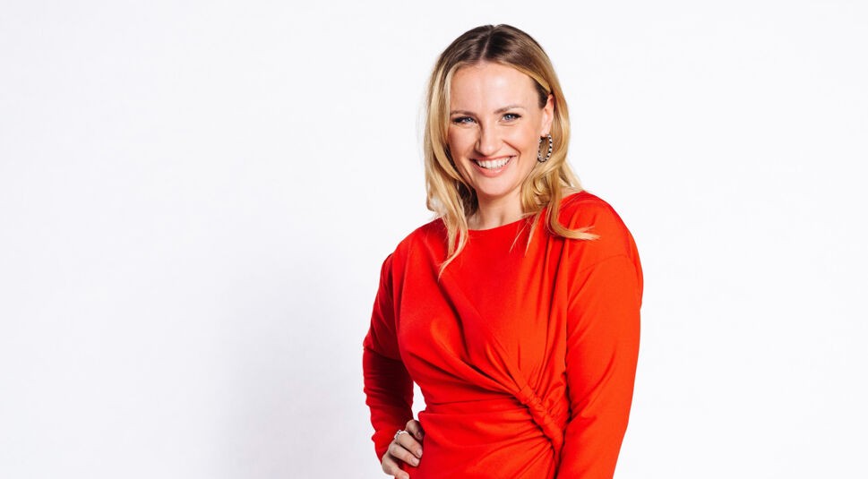 Auf dem Bild zur Alles was zählt Besetzung ist Schauspielerin Ania Niedieck zu sehen, die in der Serie die Rolle der Isabelle Reichenbach spielt. Sie trägt ein elegantes, knallrotes Kleid mit raffiniertem Faltenwurf, ihr blondes Haar fällt locker über die Schultern. Mit einem strahlenden Lächeln blickt sie direkt in die Kamera, der Hintergrund ist schlicht weiß gehalten.