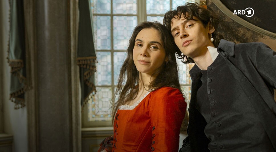 Auf dem Bild in den GigaTV-Highlights im Dezember 2025 siehst du eine Szene aus „Mozart/Mozart“: Wolfgang Amadeus Mozart (Eren M. Güvercin) und seine Schwester Nannerl (Havana Joy) posieren in historischer Kleidung vor einem Fenster mit Bleiglas.