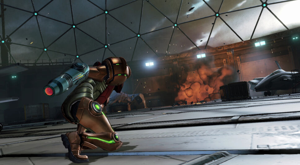 Im Bild zu Metroid Prime 4: Beyond Tipps kniet Samus Aran mit erhobenem Armkanone in einem futuristischen Hangar, während im Hintergrund eine Explosion für Chaos sorgt. Ihre Rüstung leuchtet an mehreren Stellen grün und wirkt kampfbereit. Trümmer und Flugzeuge verstärken die dramatische Atmosphäre der Szene.