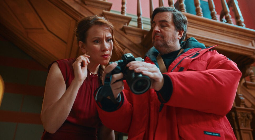 Auf dem Bild in dem Artikel zu "Fabian und Die mörderische Hochzeit" zeigt ein Mann in roter Winterjacke einer Frau eine Kamera.