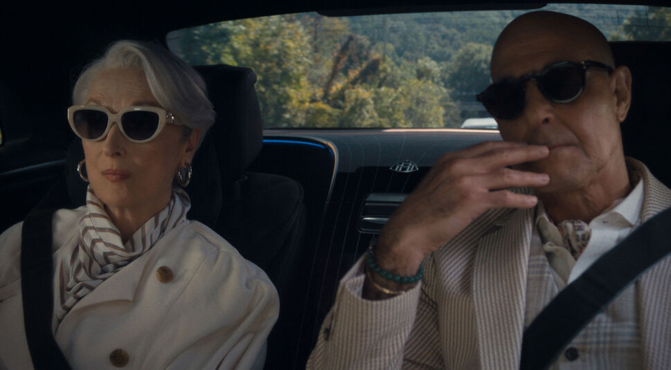 Auf dem Bild zu Der Teufel trägt Prada 2 sind Miranda Priestly, gespielt von Meryl Streep, und Nigel, dargestellt von Stanley Tucci, auf der Rückbank eines luxuriösen Autos zu sehen. Beide tragen elegante Outfits und dunkle Sonnenbrillen. Miranda sitzt ruhig und selbstbewusst links. Nigel wirkt konzentriert rechts neben ihr. Die Szene wirkt exklusiv und strahlt Macht sowie modische Autorität aus.