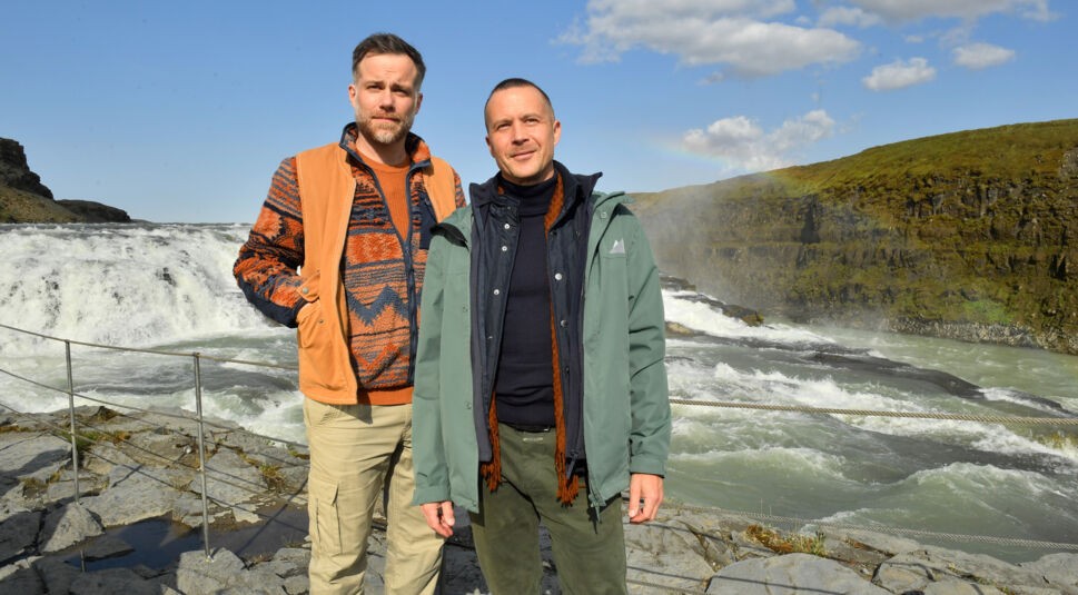 Am Gullfoss Wasserfall: Nikolaus Andresen (Barnaby Metschurat) und Dominik Dahlke (Bernhard Piesk) stehen nebeneinander an der Absperrung des Wasserfalls. Sie blicken lächelnd in die Ferne. Über dem Wasserfall hat sich Regenbogen gebildet.