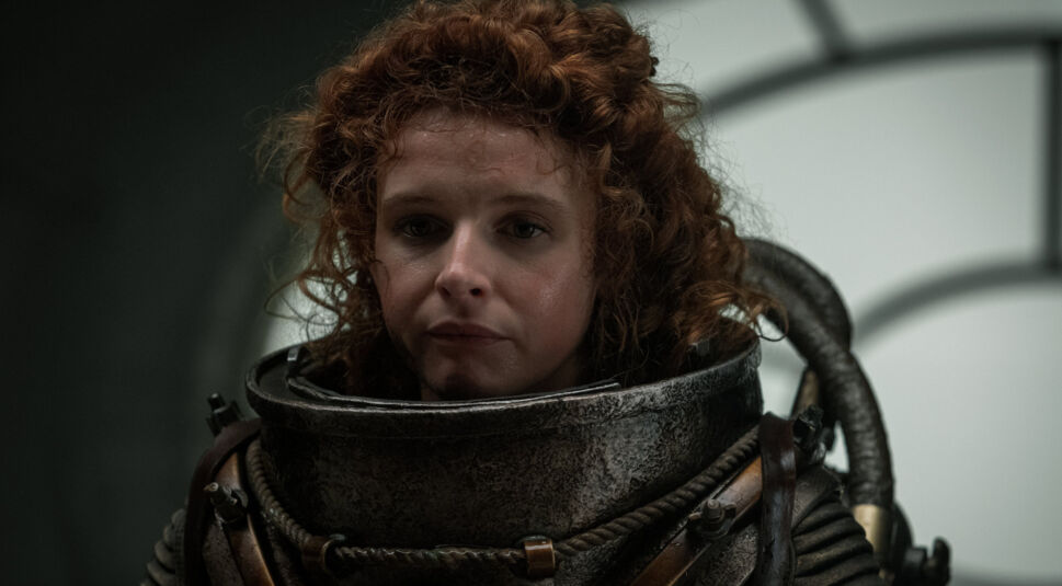 Humility (Georgia Flood) hält sich in einem Tauchanzug in einem Raum auf.