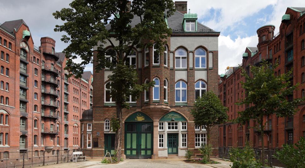 Historisches Backsteingebäude in der Hamburger Speicherstadt mit grünen Türen und Fenstern; das Teekontor aus „Die Pfefferkörner“, umgeben von Fleeten und weiteren roten Speicherhäusern.