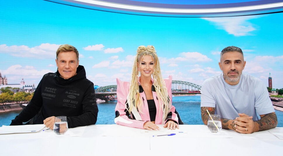 Auf dem Bild in den GigaTV-Highlights im April 2026 siehst Du die Jury von DSDS 2026 mit Dieter Bohlen, Rapper Bushido und Schlagersängerin Isi Glück. Sie sitzen nebeneinander an einem Tisch vor einer hellen Studiokulisse. Alle blicken freundlich in die Kamera, die Atmosphäre wirkt professionell, modern und zugleich unterhaltsam.