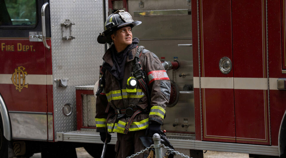 Auf dem Bild zu den GigaTV Highlights im Mai 2026 aus der Serie Chicago Fire ist Lieutenant Kelly Severide, gespielt von Taylor Kinney, in voller Feuerwehrmontur zu sehen. Er steht vor einem roten Feuerwehrfahrzeug, blickt aufmerksam zur Seite und wirkt konzentriert sowie einsatzbereit. Die Szenerie vermittelt eine angespannte, dynamische Stimmung während eines möglichen Rettungseinsatzes im urbanen Umfeld.