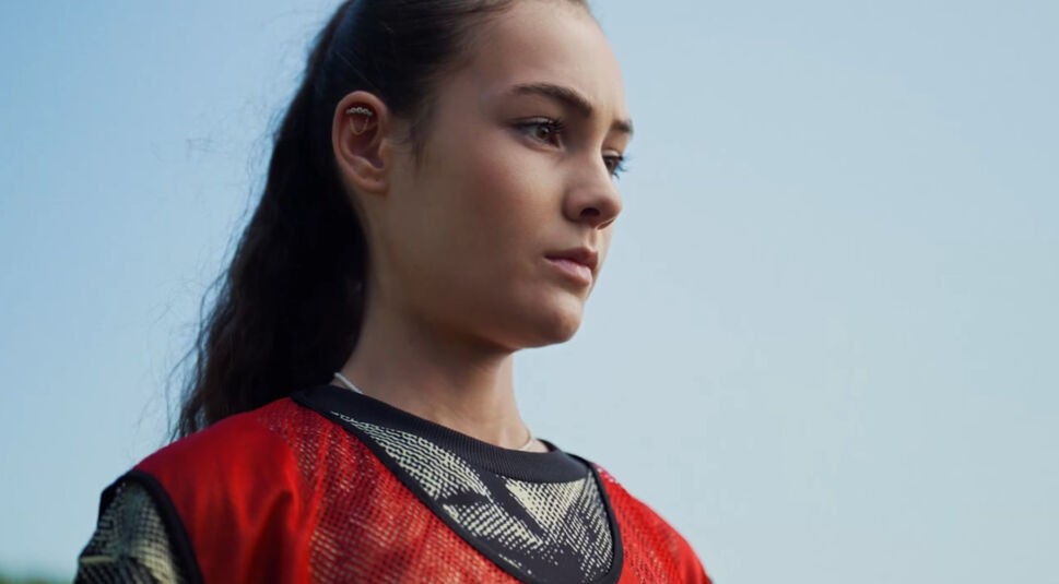 Auf diesem Bild zur Vodafone-Kampagne "Search like a Champion" ist eine Jugendliche mit einem roten Fußballl Trikot zu sehen. Sie schaut fokussiert nach vorn und konzentriert sich auf ihren nächsten Schuss.