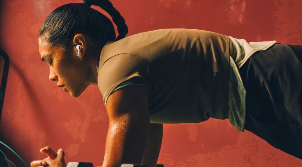 Frau mit AirPods Pro 3 in den Ohren macht Sport auf einer Matte.