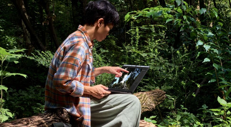 Junger Mann arbeitet im Wald an seinem MacBook Pro.