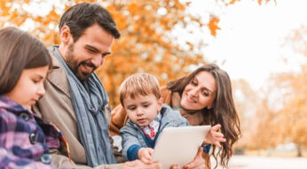 Smiling parents teaching their children how to use touchpad outdoors.