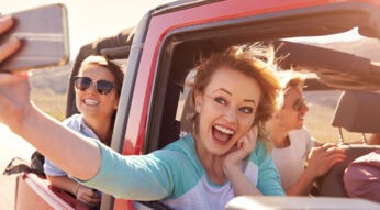 Friends On Road Trip In Convertible Car Taking Selfie