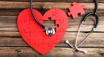 Red puzzle heart with stethoscope on brown wooden background