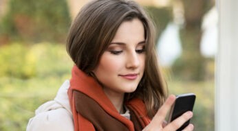 Junge Frau mit orangem Schal schaut auf ihr Smartphone.