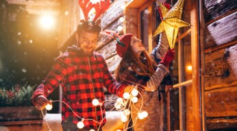 Junges Paar hängt leuchtende Weihnachtsdekoration auf