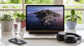 MacBook, Smartphone und Kopfhörer auf einem Schreibtisch am Fenster