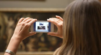 Frau in Augmented-Reality-Ausstellung sieht mit dem Smartphone digitale Kunst an.