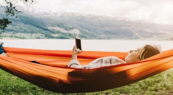 Frau nutzt Lese-Apps in Hängematte am See