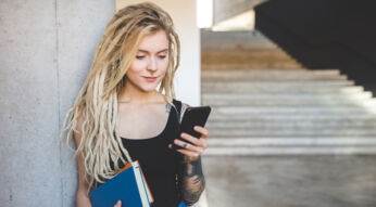 Eine Frau lehnt mit Smartphone in der Hand an einer Wand