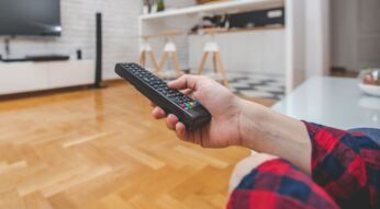 Junger Mann schaltet mit seiner Fernbedienung einen neuen deutschen Film ein.