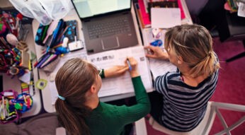 Eine Mutter lernt mit ihrer Tochter am Schreibtisch vor einem Notebook für die Schule.
