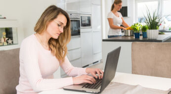 Junge Frau sitzt konzentriert mit Laptop an Tisch in Wohnküche