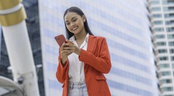 Frau mit rotem Blazer schaut lächelnd auf ihr iPhone.