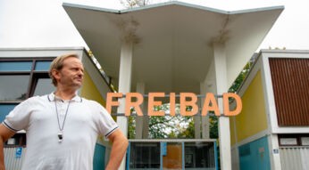 Bademeister Karl steht vor dem Freibad-Schild
