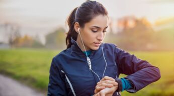 EIne Frau in Sportkleidung prüft draußen ihre Smartwatch.