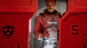 Ein Mann in einem Raumanzug am Schott einer Raumstation