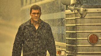 Jack Reacher (Alan Ritchson) steht im Regen neben einem Bus
