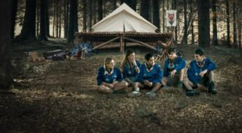 Fünf junge Pfadfinder:inen sitzen vor einem Zelt im Wald.