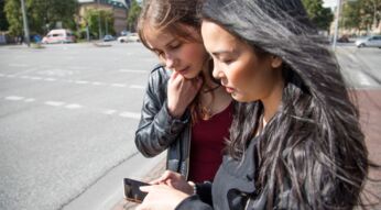 Zwei junge Frauen an Straßenkreuzung schauen auf ein Smartphone