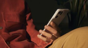 Sitzende Person hält das Smartphone OPPO Find X5 Pro lässig auf dem Knie abgestützt, warme Farben