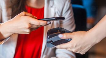 Frau hält Smartphone zum Bezahlen über Lese-Gerät