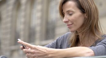 Frau steht draußen und schaut lächelnd auf ihr Smartphone