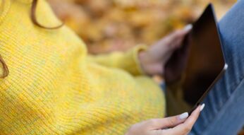 Frau mit gelbem Pullover hält iPad Pro 2021 im herbstlichen Park