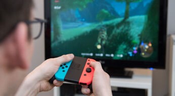 Mann vor Fernseher spielt Computerspielt mit Joy Cons der Nintendo Switch
