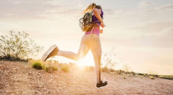 Sportliche Frau mit Rucksack läuft in Sonnenuntergang