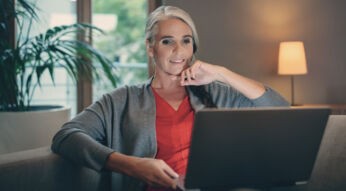 Frau schaut auf Laptop, der auf dem Schoss liegt.