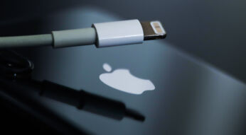 Lightning-Kabel vor schwarzem iPhone mit weißem Apple-Logo auf der Rückseite