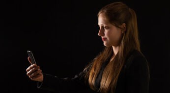 Junge Frau im Profil mit langen Haaren guckt auf ihr iPhone zur Gesichtsentsperrung