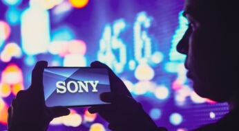 Mann vor bunten Leuchttafeln hält Handy mit beiden Händen, auf dem Display das Sony-Logo