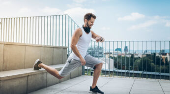 Junger Mann auf Dach trainiert an Stufen aus Stein und schaut lächelnd auf seine Smartwatch